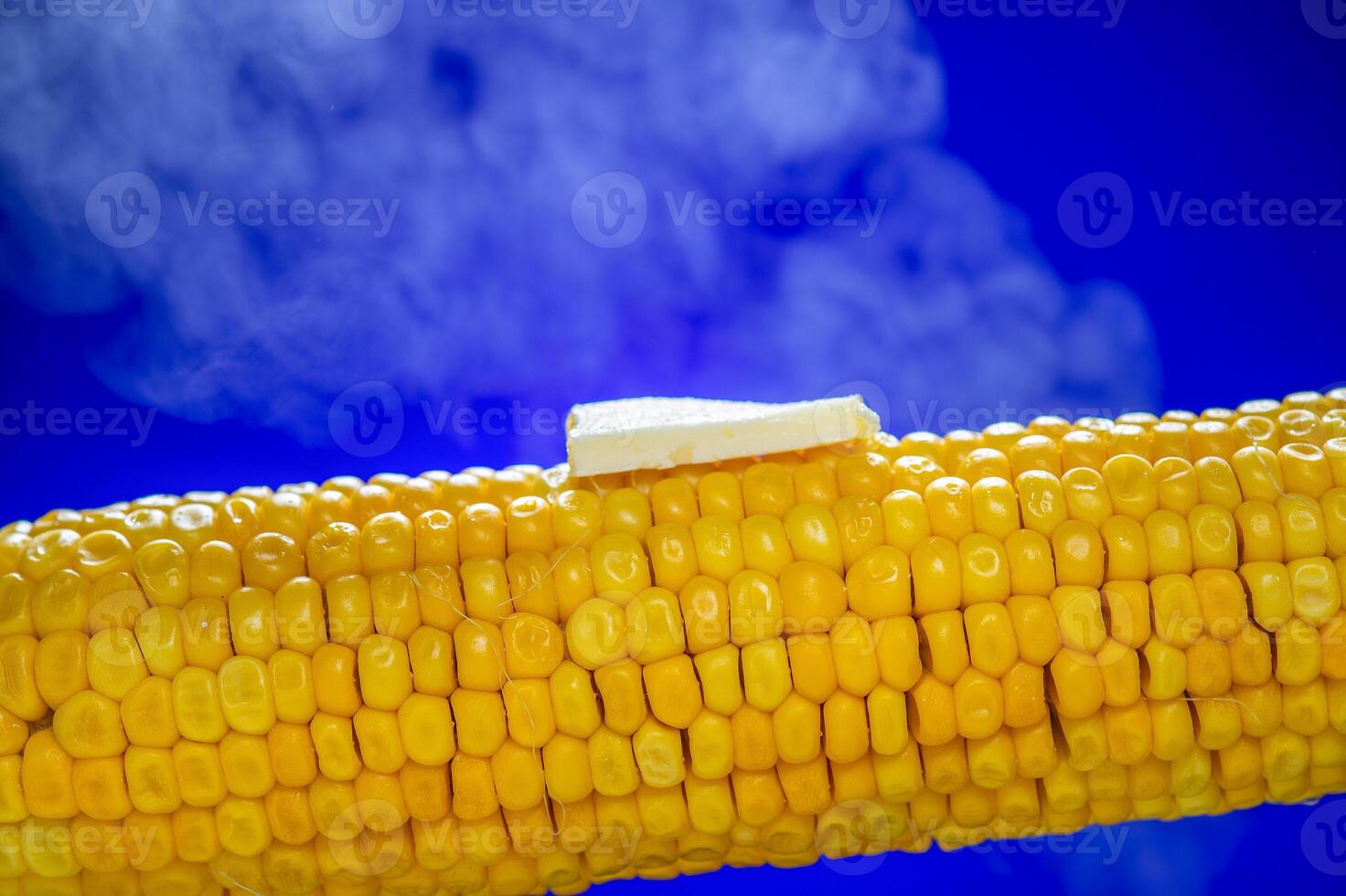Delicious yellow corn on the cob with a melting piece of butter on top, placed against a vibrant blue background. photo