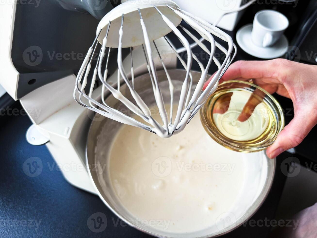 Making dough in a planetary mixer. Women's hands pour oil into a bowl with dough. Cooking at home. photo