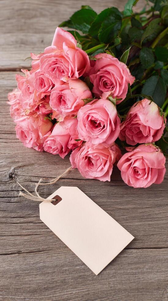 Beautiful Pink Roses Arranged on Wooden Table With Blank Tag for Labeling or Gift Notes. photo