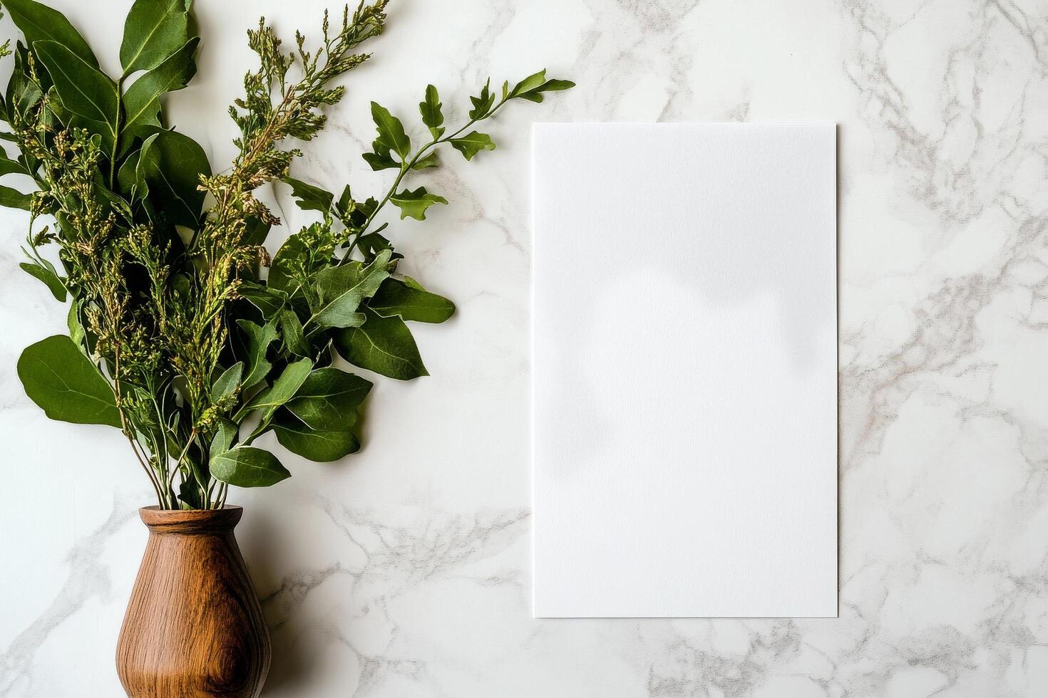 Fresh Greenery Placed in a Wooden Vase Beside a Blank Sheet of Paper on a Marble Surface photo