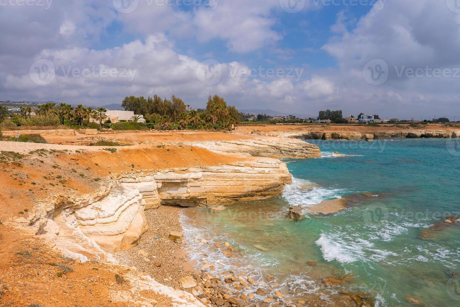 Rugged white limestone cliffs meet turquoise Mediterranean waters, with a pebble strewn beach, palm trees, and a luxury resort in the background. photo