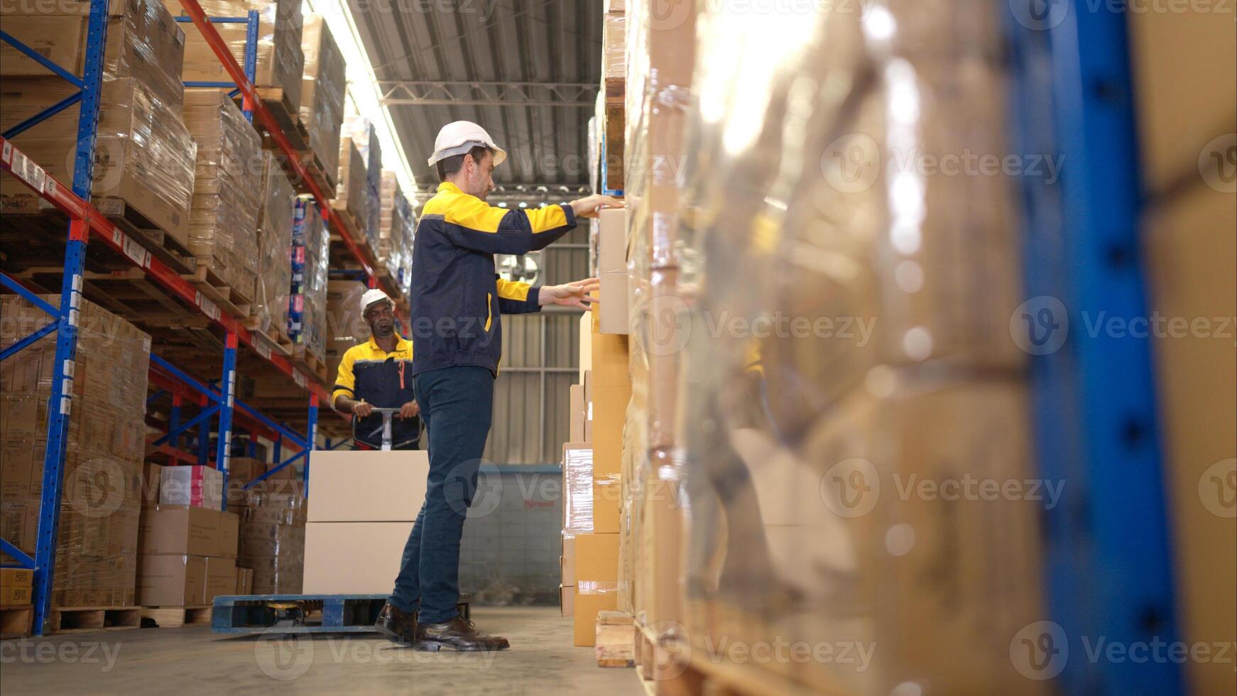 Two warehouse workers are lifting boxes of merchandise on a pallet jack to store on a shelf in a warehouse,70 photo