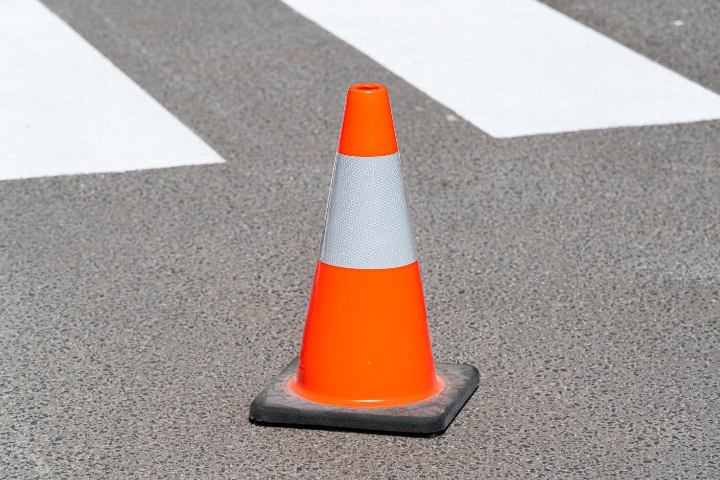 Traffic cone, with white and orange stripes on gray asphalt. Construction cone. Symbol of restrictions, roadworks, attention photo