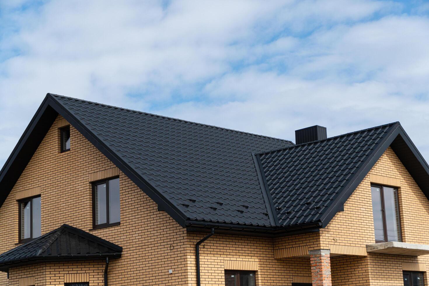 New brick house. The modern house with plastic windows and a black roof of corrugated sheet. Metal roofing photo