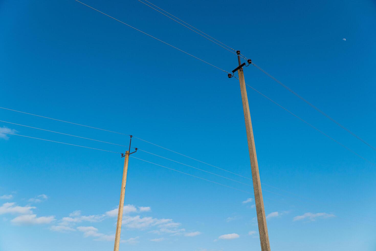 The line of electric poles with cables of electric against blue sky with clouds. Concept of power line with electrical poles photo