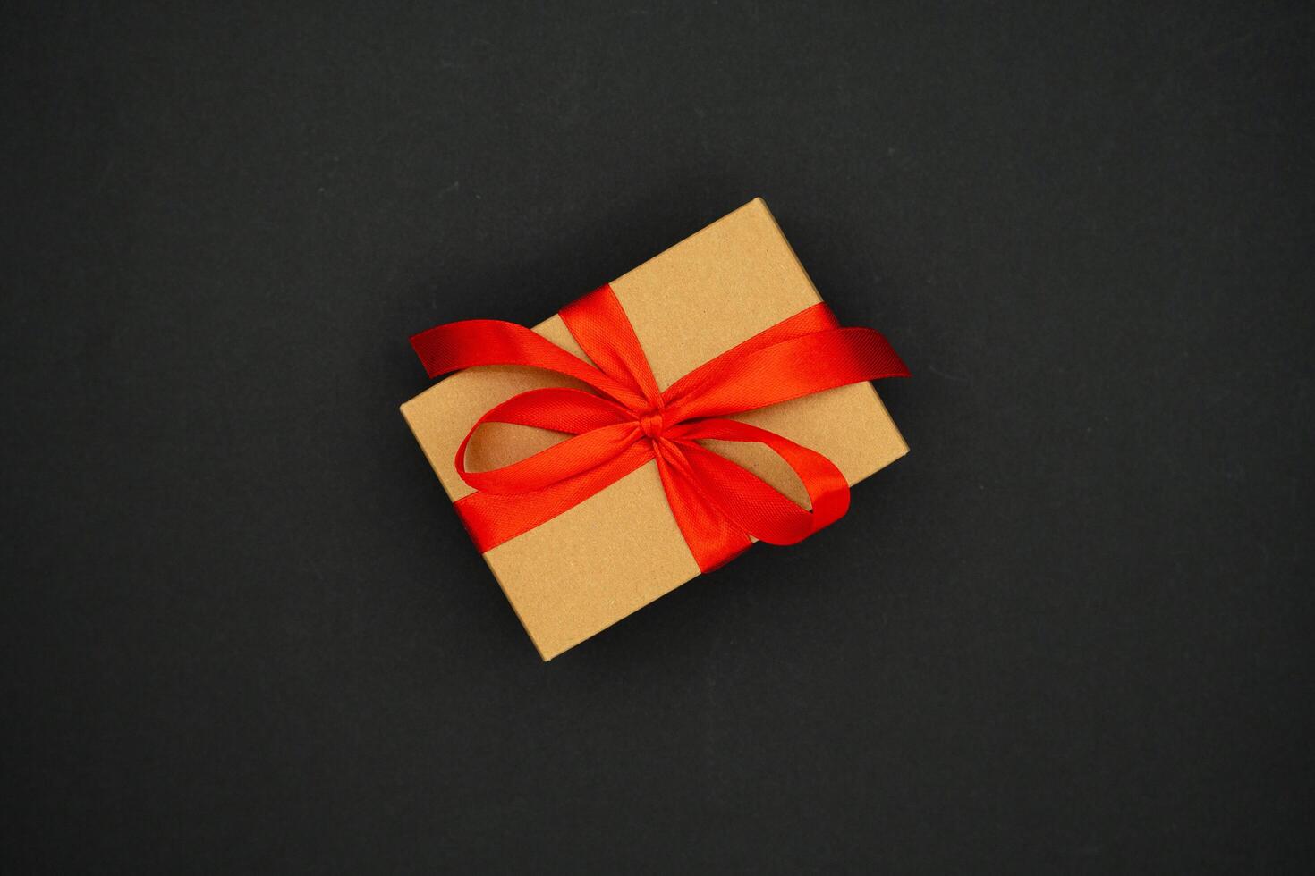 Present box from brown paper with red ribbon bow, isolated on black background. Celebration concept photo