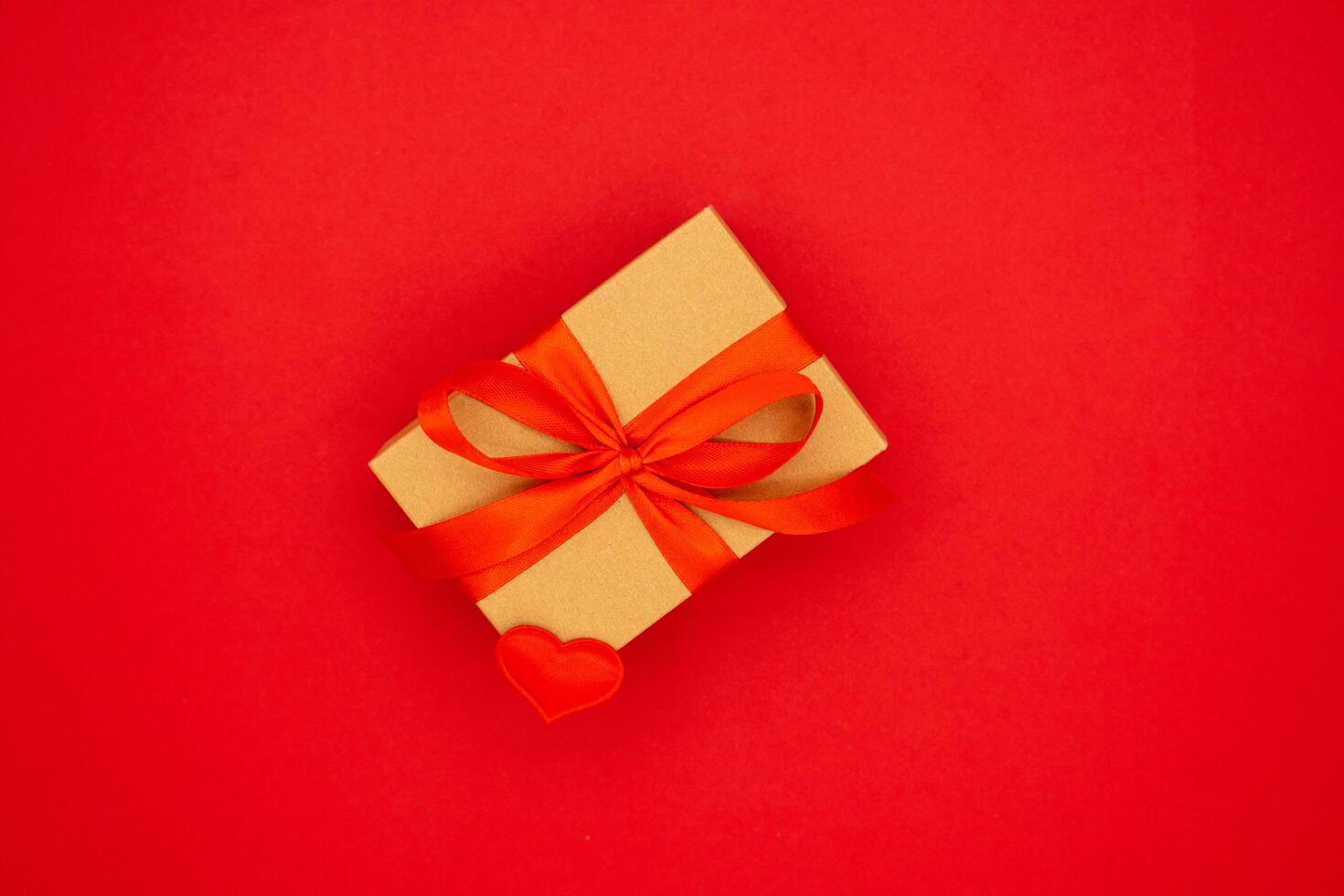Wrapped brown present box with red ribbon bow, isolated on red. The concept of the holidays photo