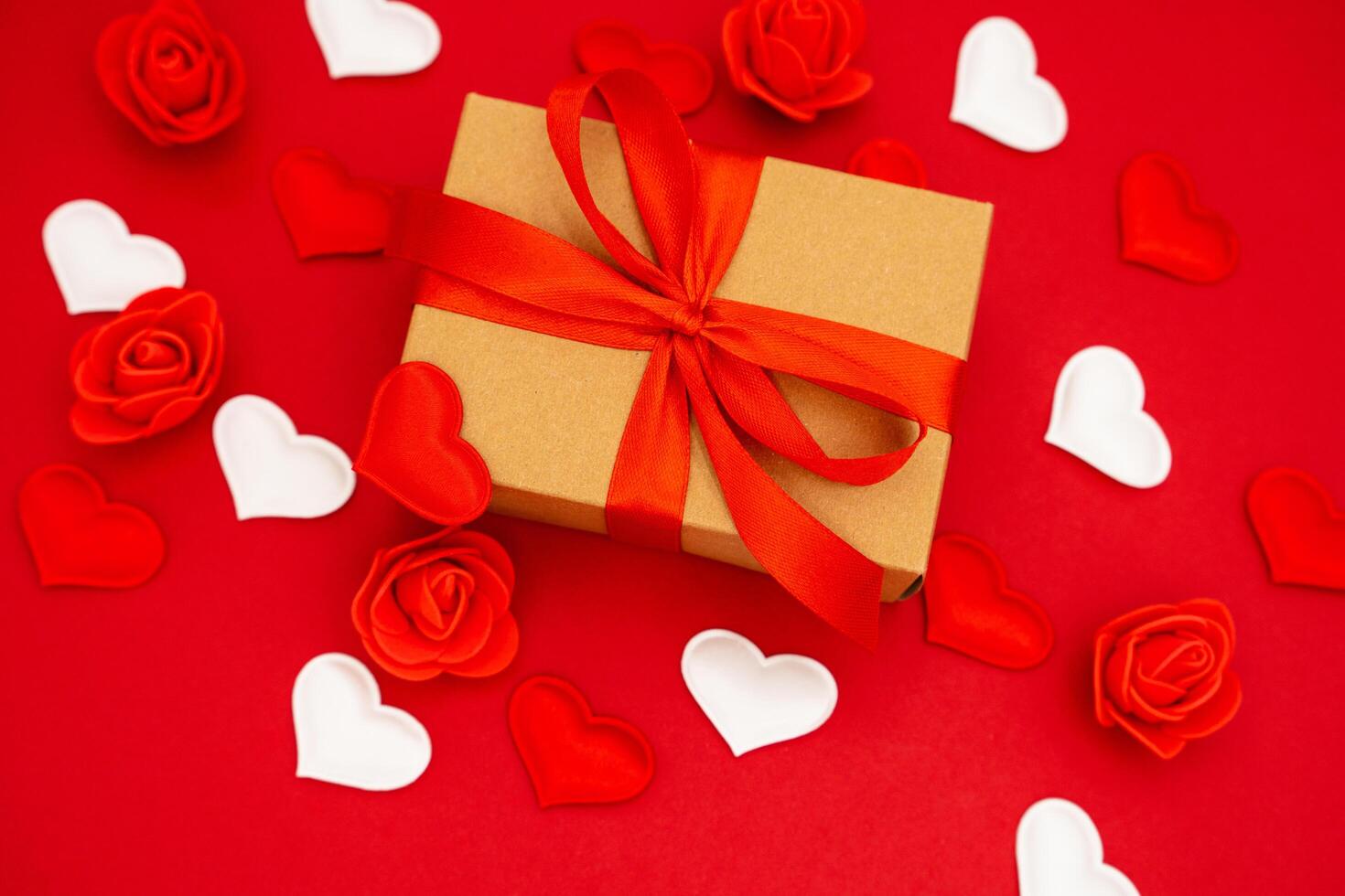 Valentine's Day. Gift box of kraft paper with a red ribbon. Red background with hearts and roses around photo