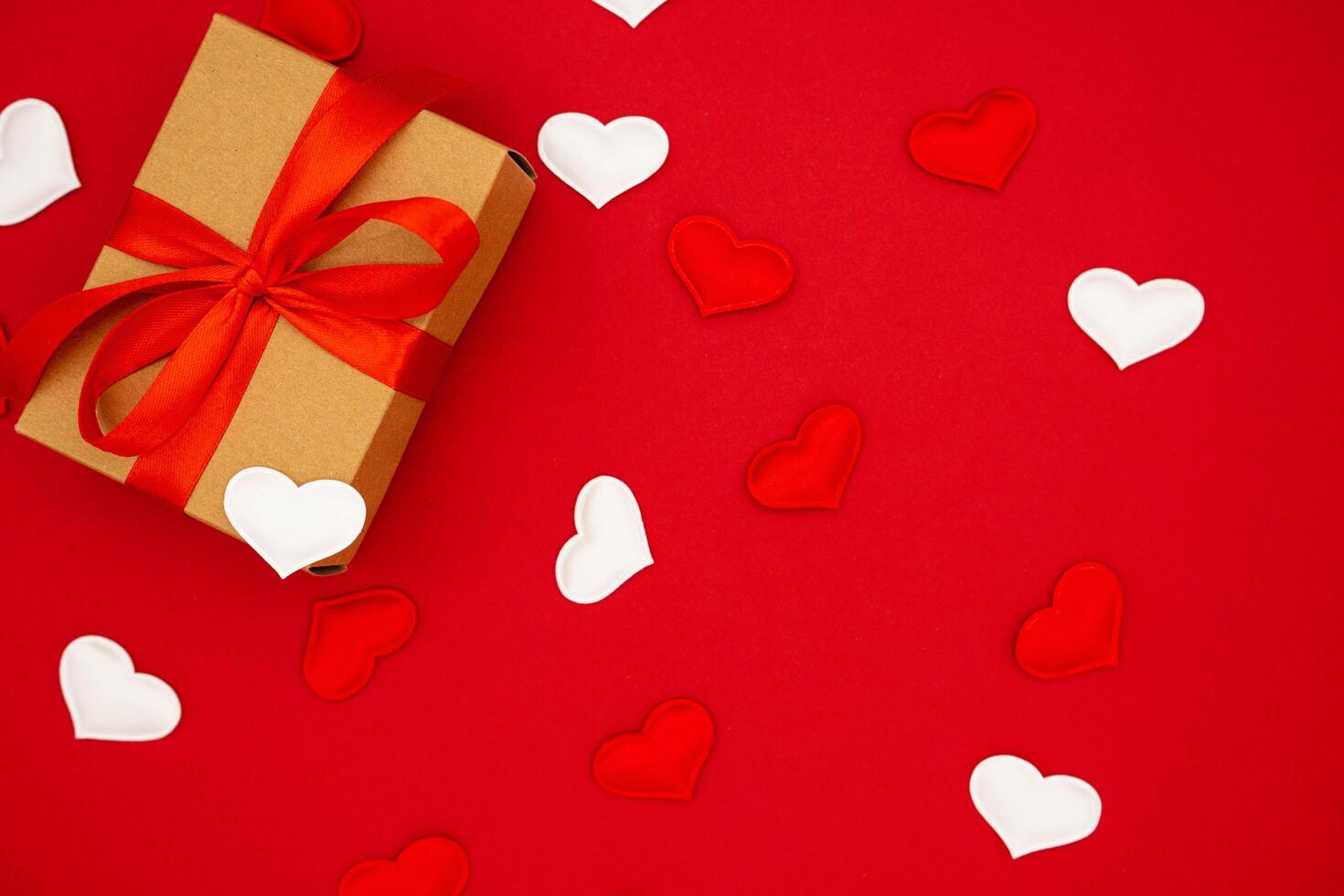 Valentine's Day background. Gift box of kraft paper with red bow on red background with hearts. Place for text, banner. photo