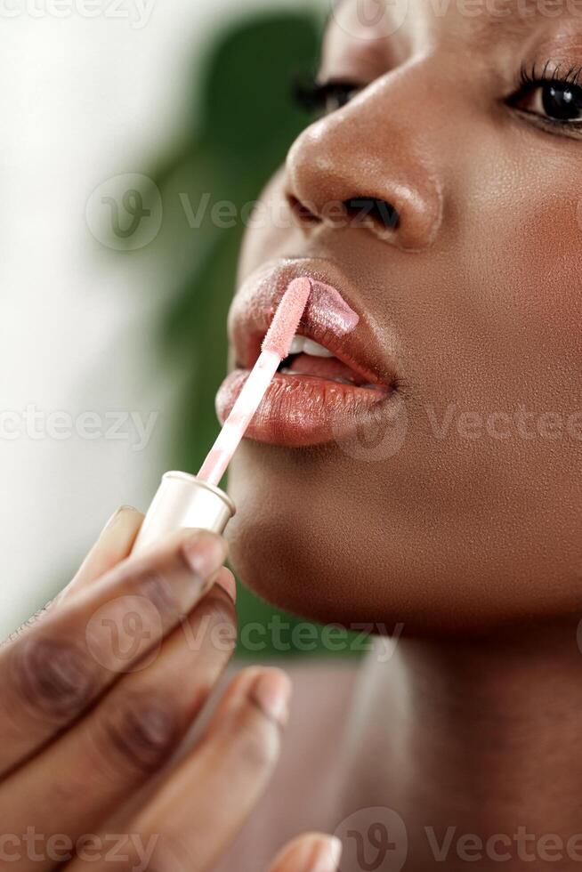 Woman applying lip gloss in bright indoor setting with lush greenery in the background photo