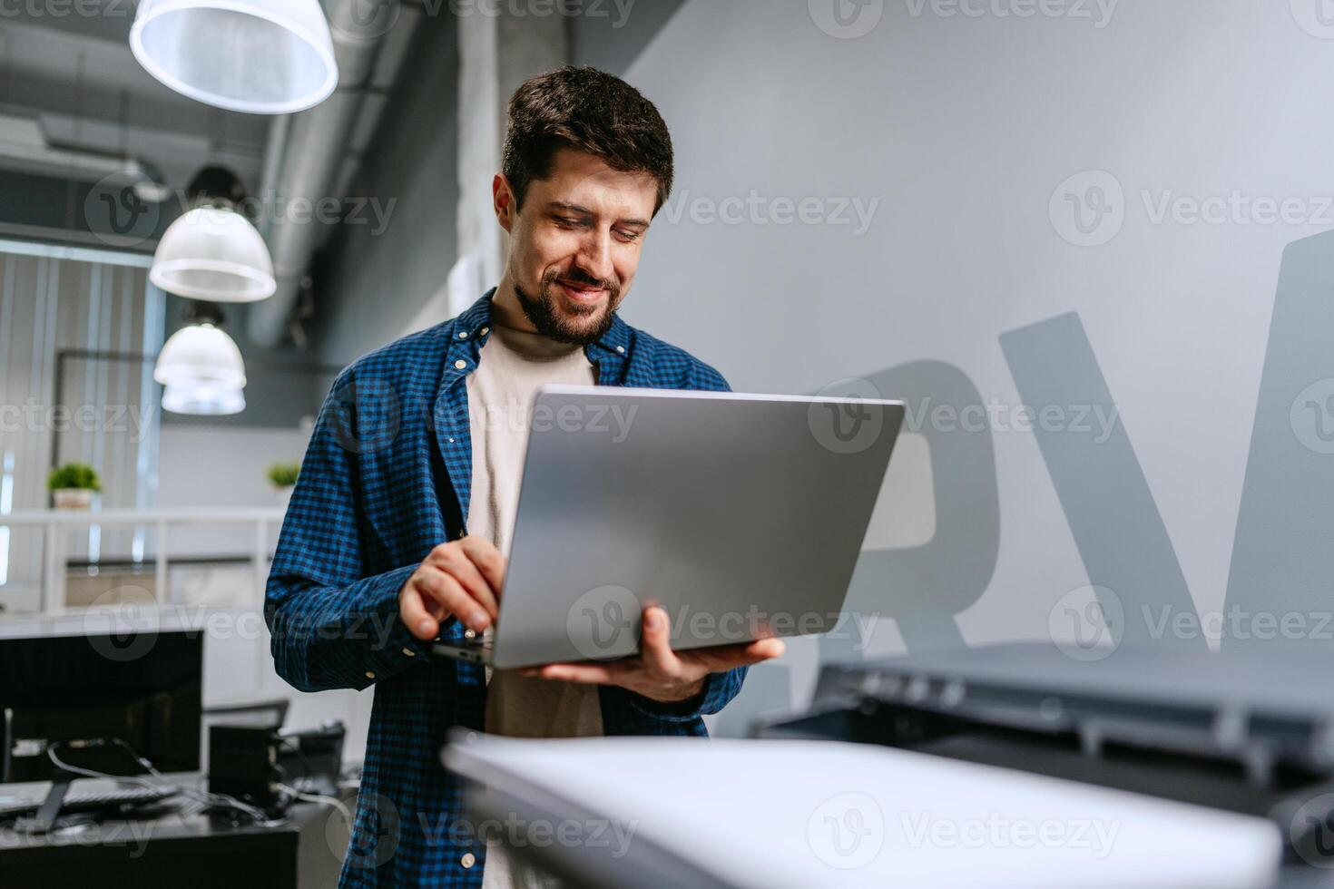 Man working on laptop in modern office environment during daytime with smiling expression photo