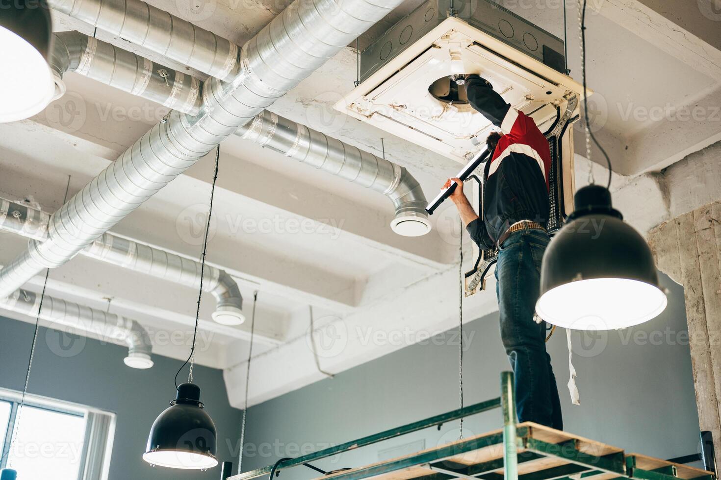 Technician performing maintenance on ceiling-mounted air conditioning unit in modern workspace photo
