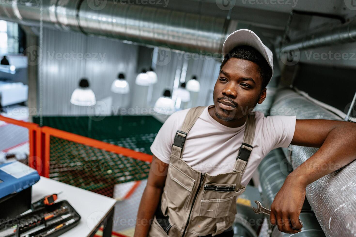 Young male technician relaxed in workshop with tools and machinery in the background during midday photo