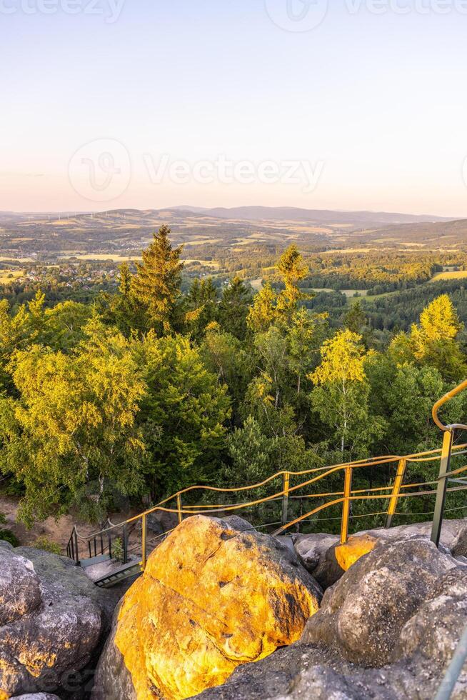Visitors enjoy the breathtaking sunset from the lookout at Popov Cliffs in the Lusatian Mountains, surrounded by lush greenery and sandstone rock formations. photo