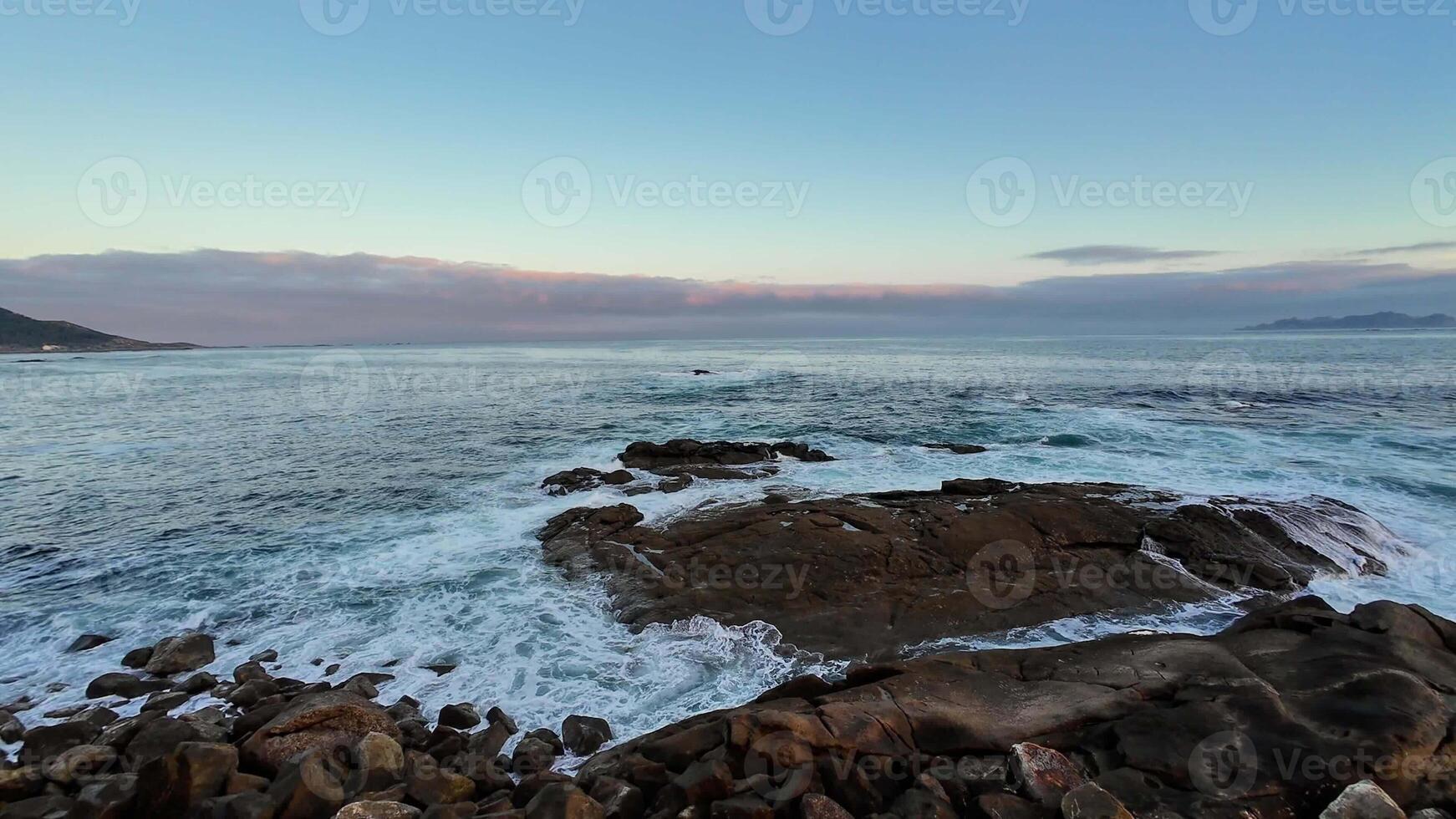 A tranquil and peaceful coastal scene featuring gentle waves lapping against rocky shores beneath a serene sunset sky photo