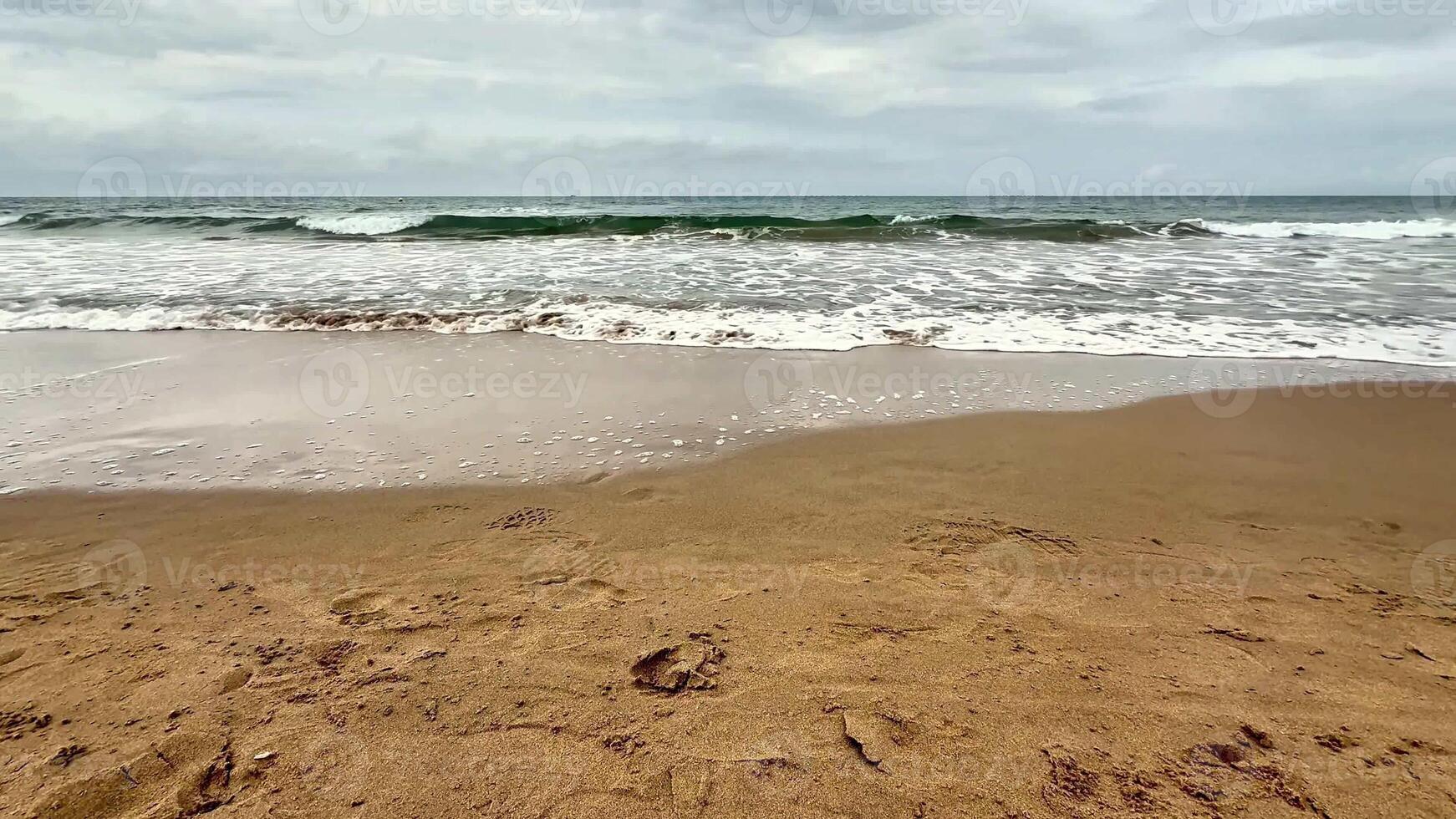 A tranquil and serene beach landscape featuring soft, golden sand, gentle waves, and overcast grey skies photo