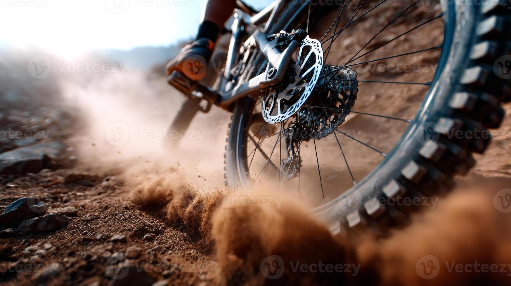 A close-up view captures the rear wheel of a mountain bike kicking up mud and dust as it navigates a rugged terrain. Afternoon sunlight enhances the action. photo
