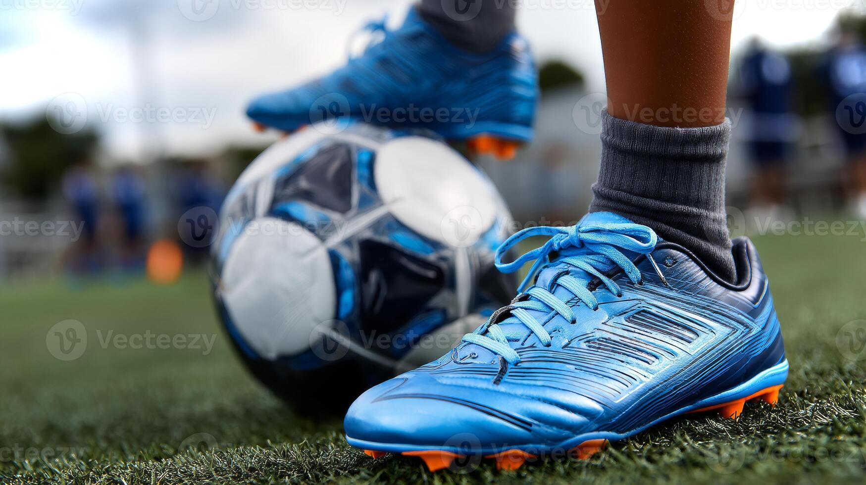 A Latino boy's foot in bright soccer cleats stands on green turf next to a soccer ball, during a practice session in the afternoon sunlight. photo