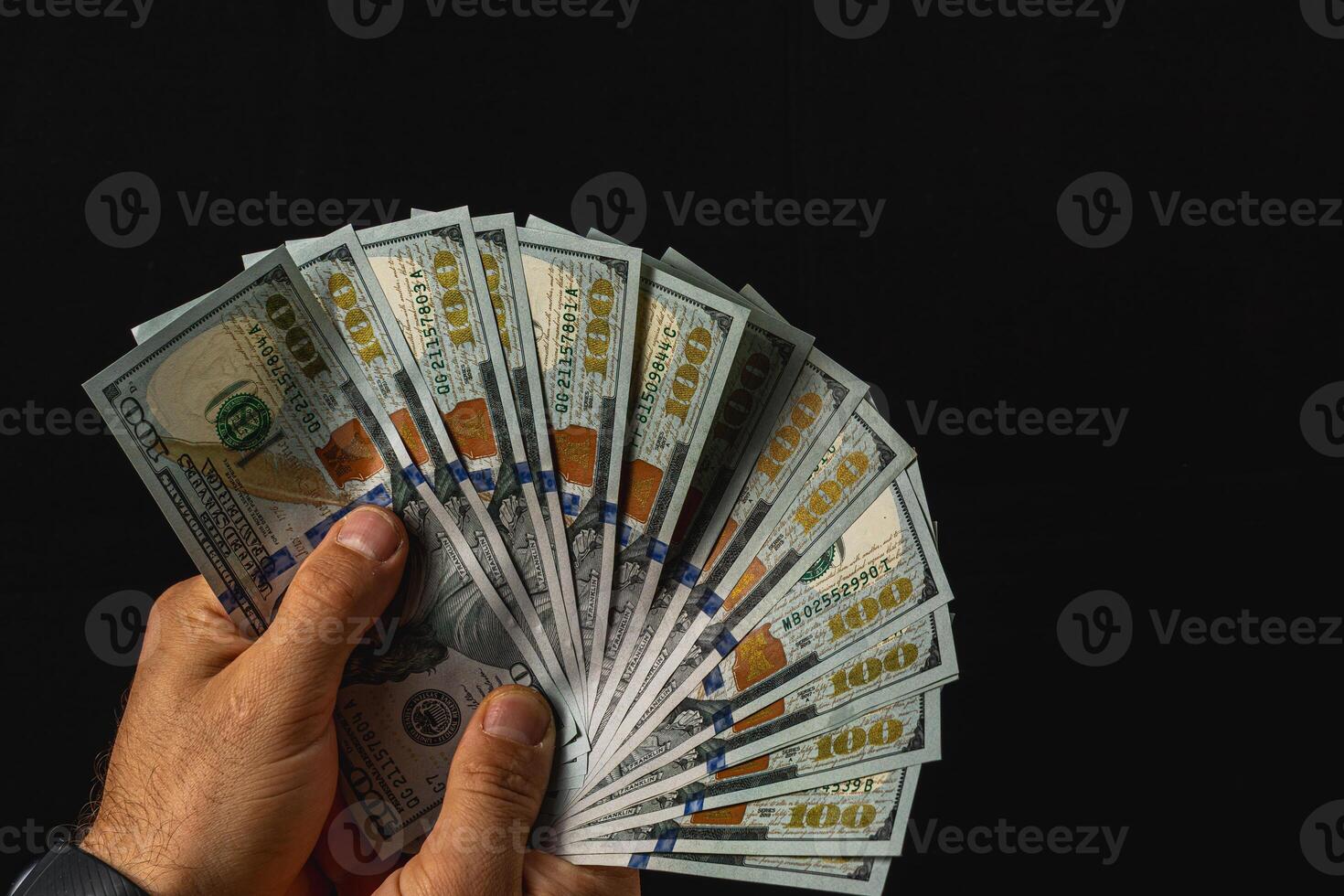 Holding a fan of hundred dollar bills against a dark background photo