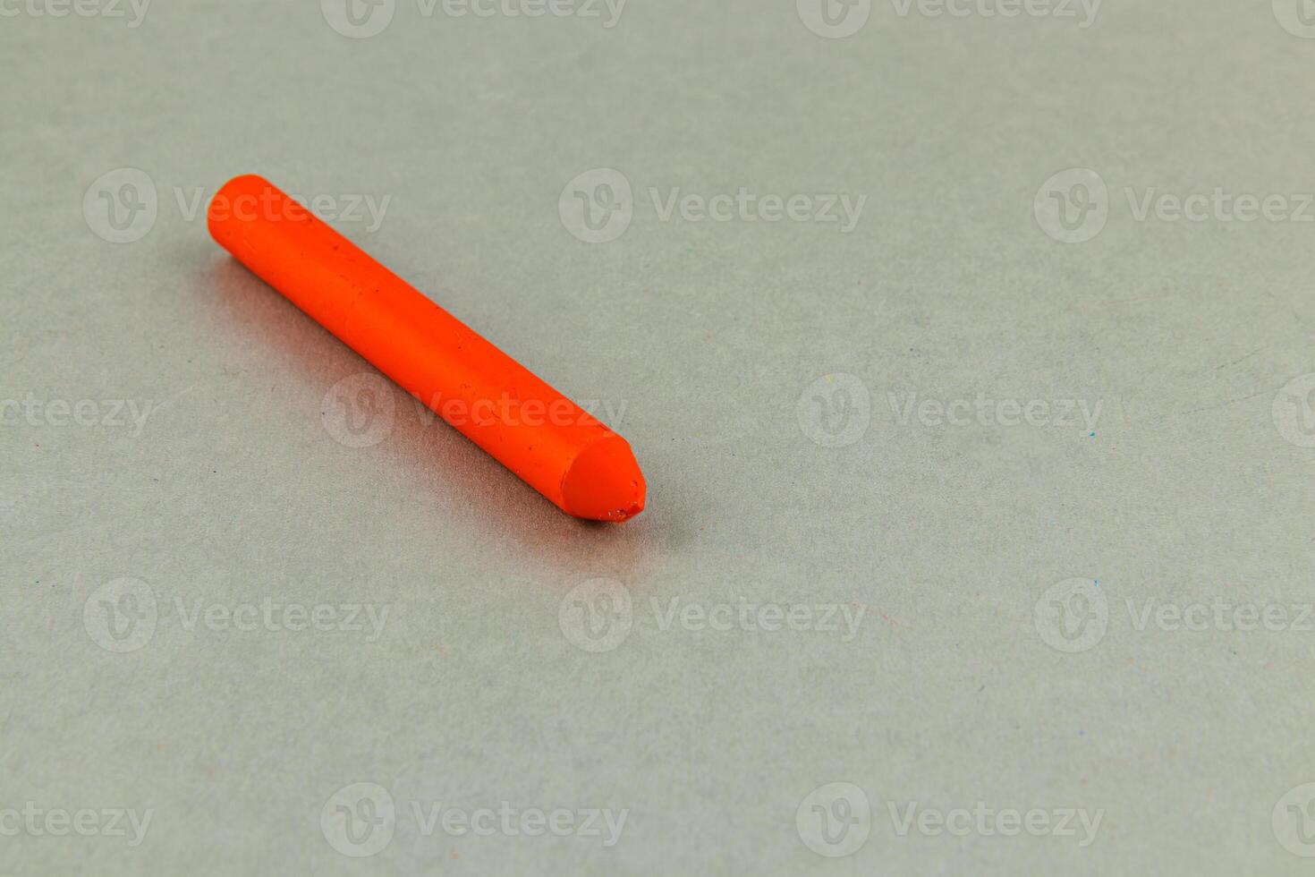 Bright orange crayon resting on a gray surface in daylight photo