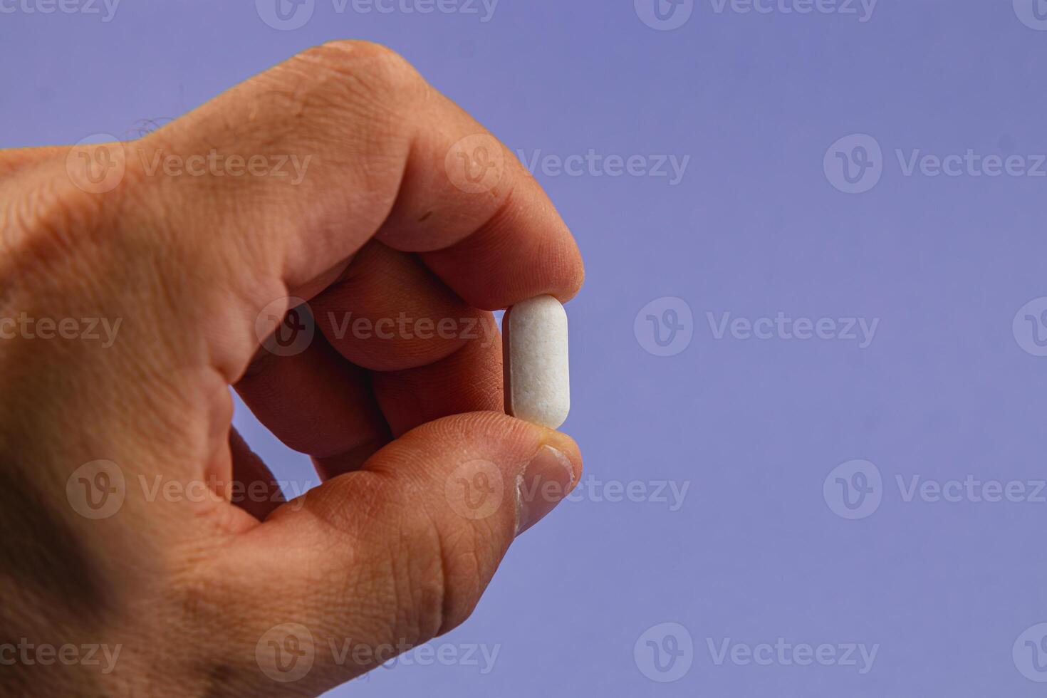 Hand holding a white pill against a purple background photo