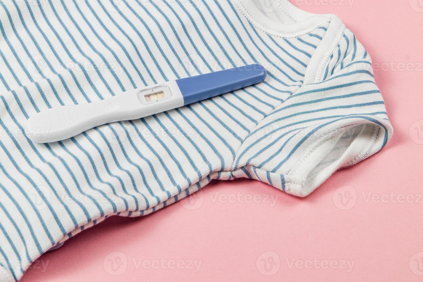 Pregnancy test on striped onesie with pink backdrop photo