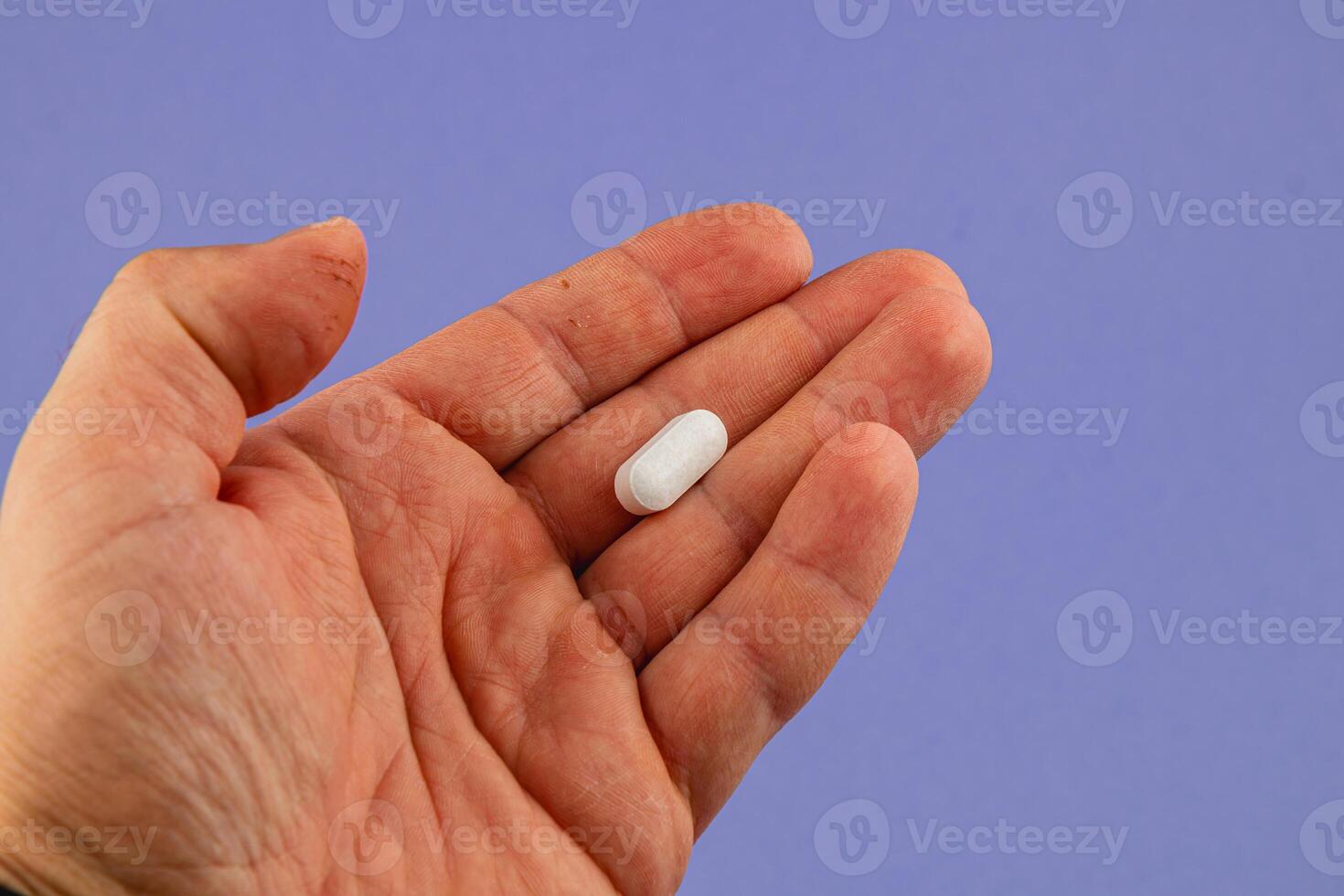 Hand holding a white pill against a blue background photo