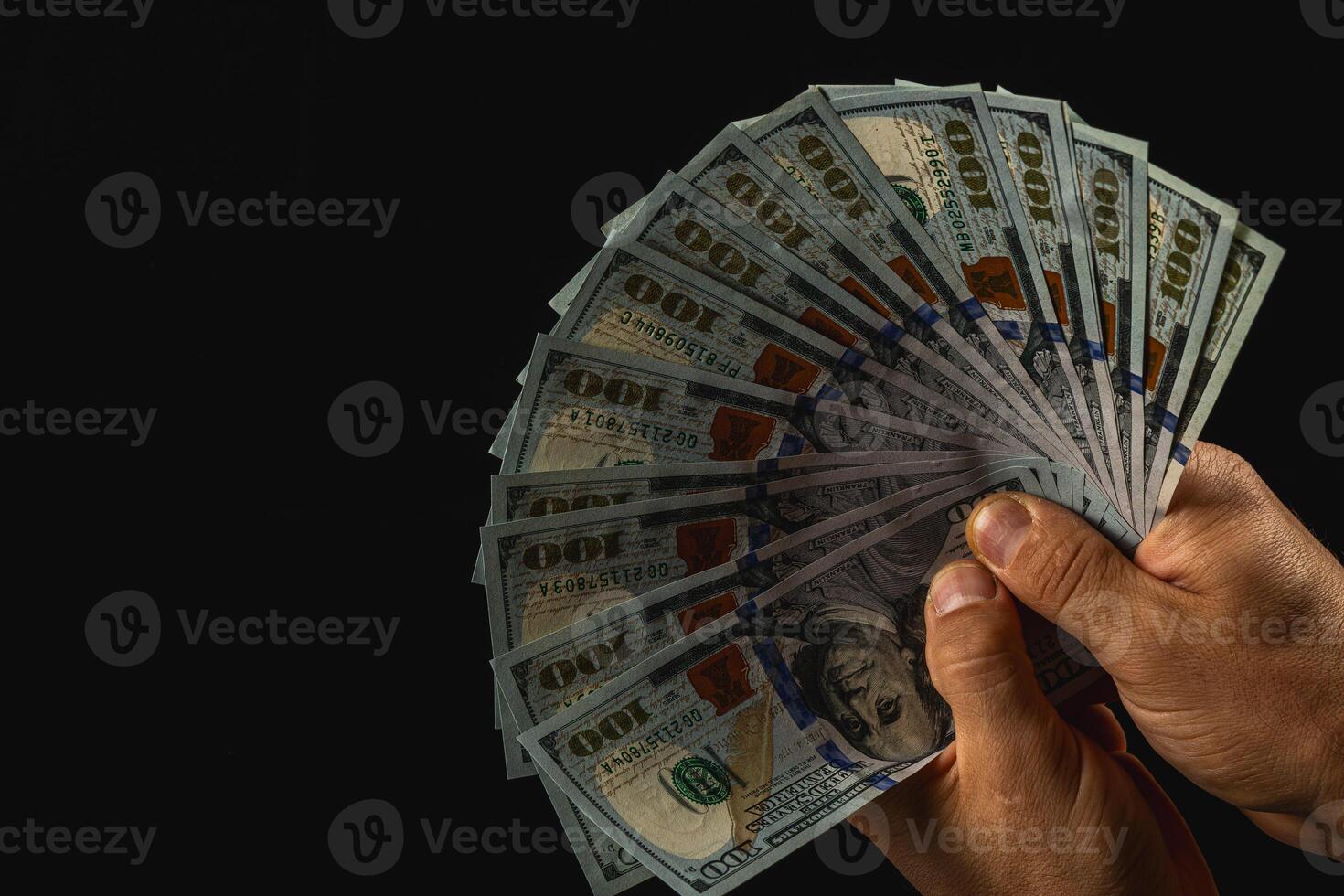 Hands displaying fanned hundred-dollar bills on black photo