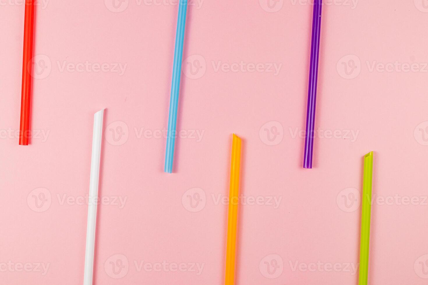 Colorful drinking straws arranged on a pink background photo