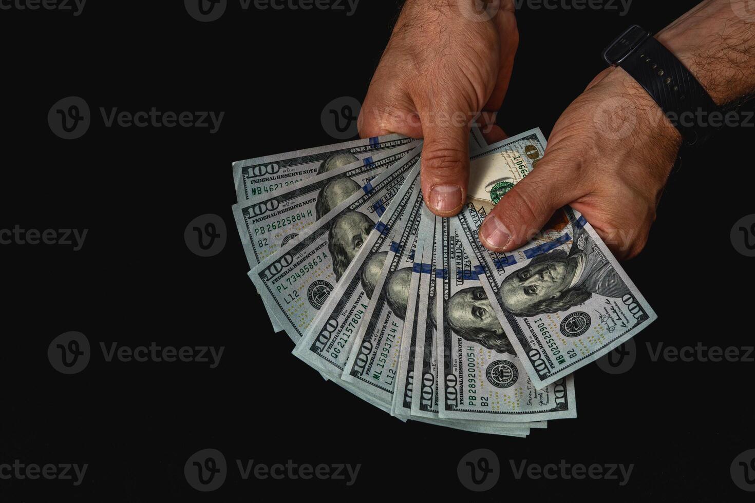 Hands displaying multiple hundred dollar bills in low light photo