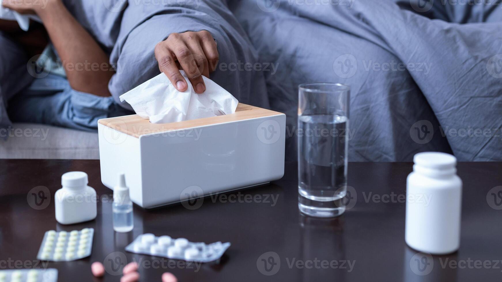 Ill African American Man Sneezing Having Sinusitis Lying On Sofa At Home. Sick Black Guy Blowing Runny Nose In Paper Handkerchief Suffering From Cold And Rhinitis Symptoms. Selective Focus photo