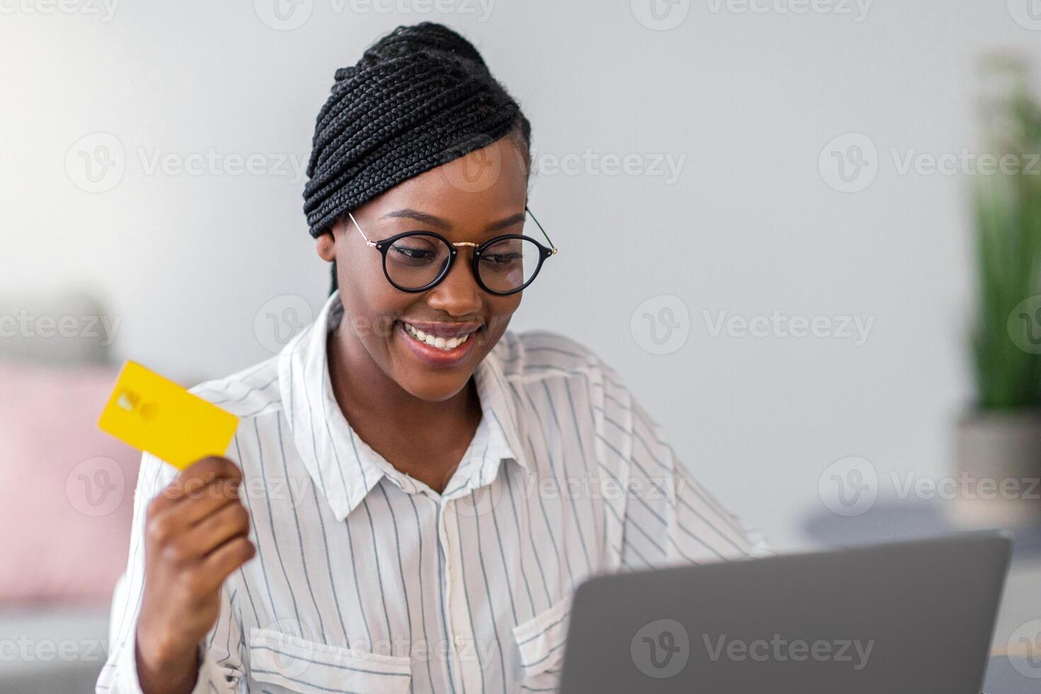 Pretty african american young woman freelancer holding credit card, using laptop, copy space. Happy black lady shopping online, ordering food, cosmetics, clothes from internet while working from home photo