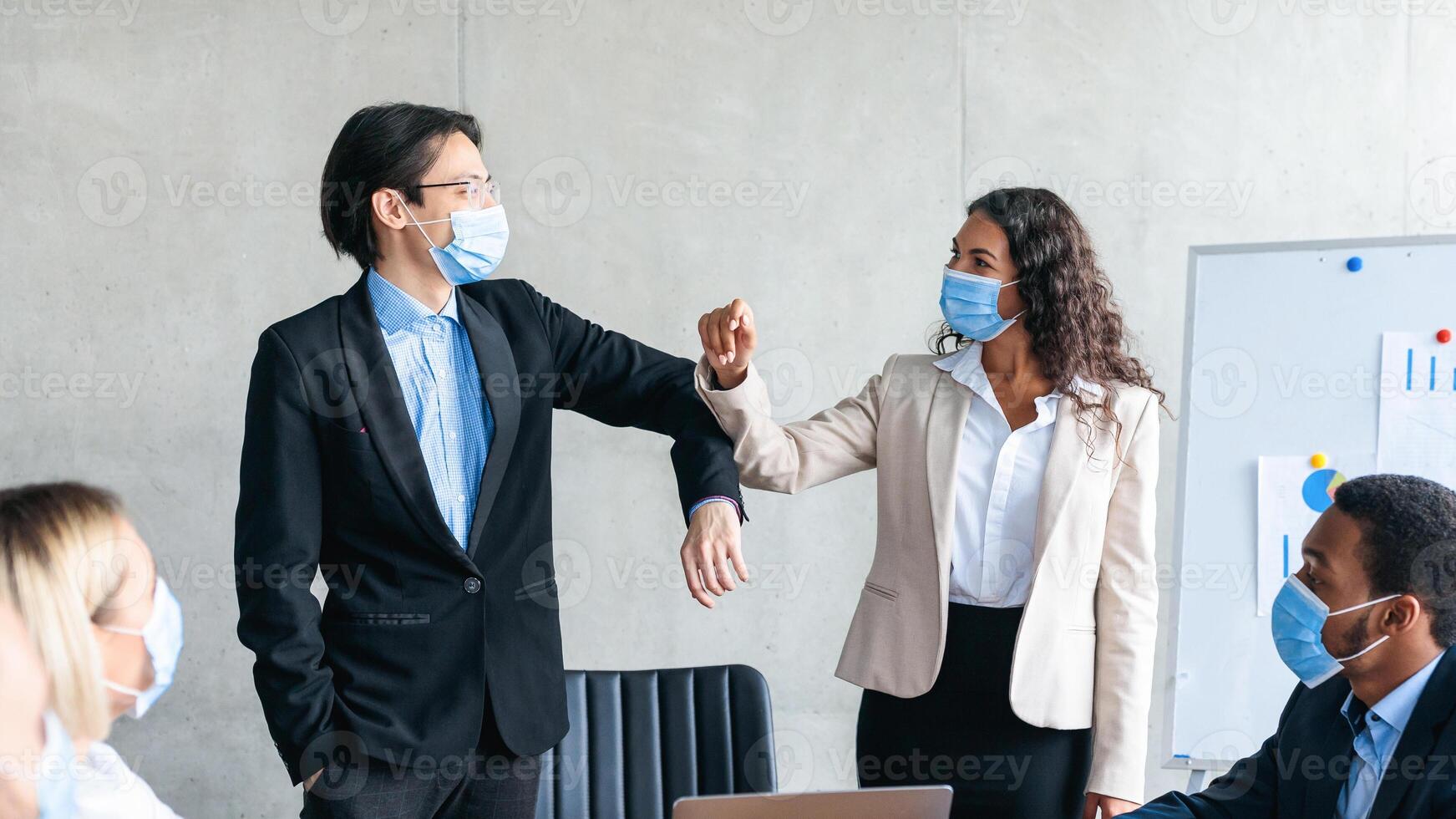 Diverse Businessman And Businesswoman Bumping Elbows Greeting Wearing Protective Face Masks During Corporate Meeting Standing In Office. Business And Covid-19 Pandemic New Rules photo