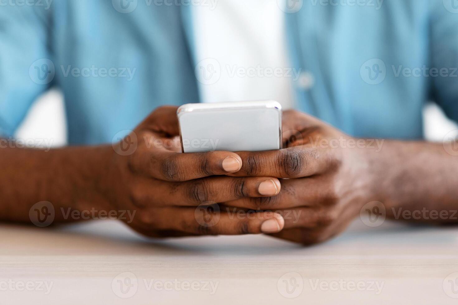 Closeup Shot Of African American Man Sitting At Desk And Using Smartphone, Cropped Image Of Unrecognizable Black Guy With Mobile Phone In Hands Texting With Somebody Or Browsing New App photo