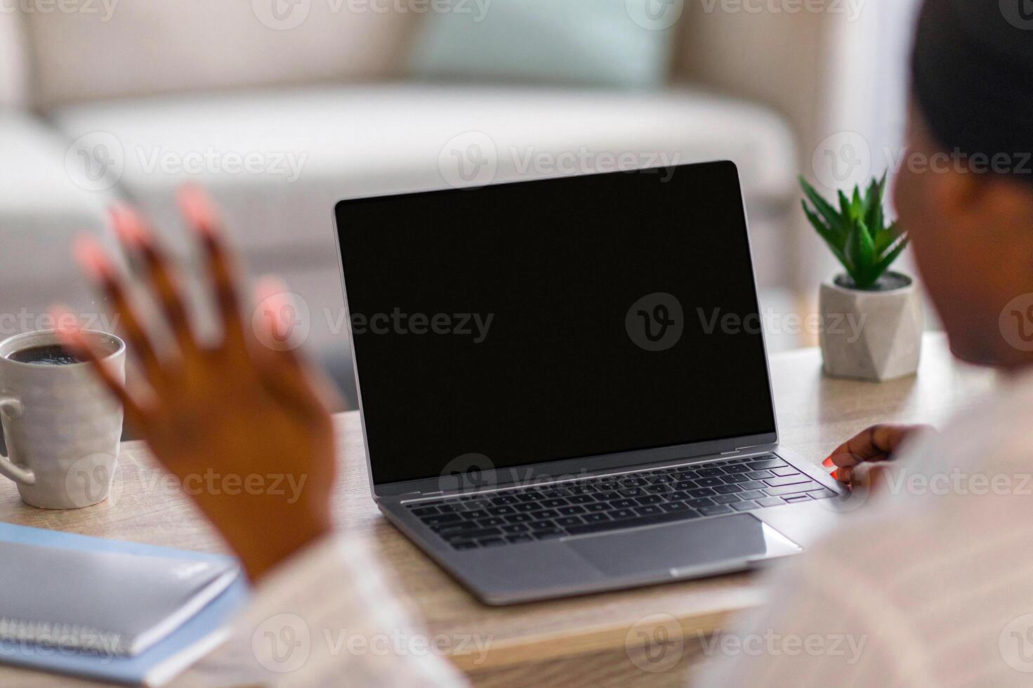 Unrecognizable black woman having chat with young man on laptop while staying home, back view, copy space. African american lady having job interview online, waving at pc screen photo