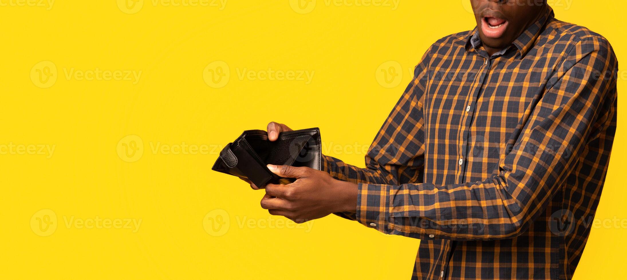 Shocked Black Guy Showing Empty Wallet At Camera, Suffering From Poverty And Absence Of Money, Emotional African Man Having Financial Crisis, Standing Isolated On Yellow Studio Background, Copy Space photo