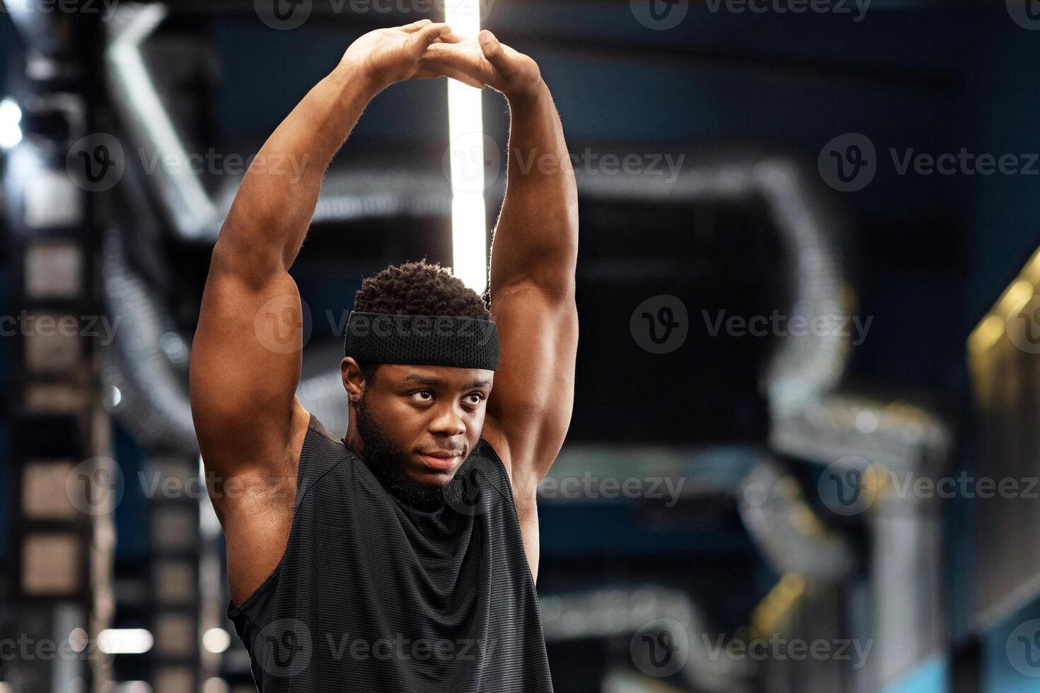 Muscular african american young man bodybuilder doing workout at gym, stretching his arms and looking at copy space. Handsome black guy sportsman getting ready before training, warming up photo