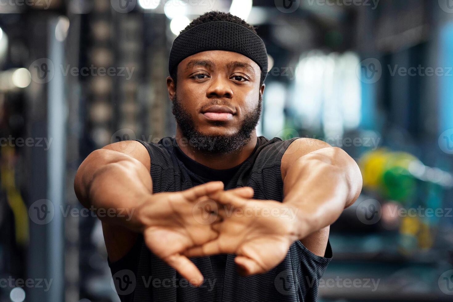 Warming up concept. Portrait of african american bearded sportsman stretching his hands before workout, muscular young black man bodybuilder training at gym, closeup, copy space photo