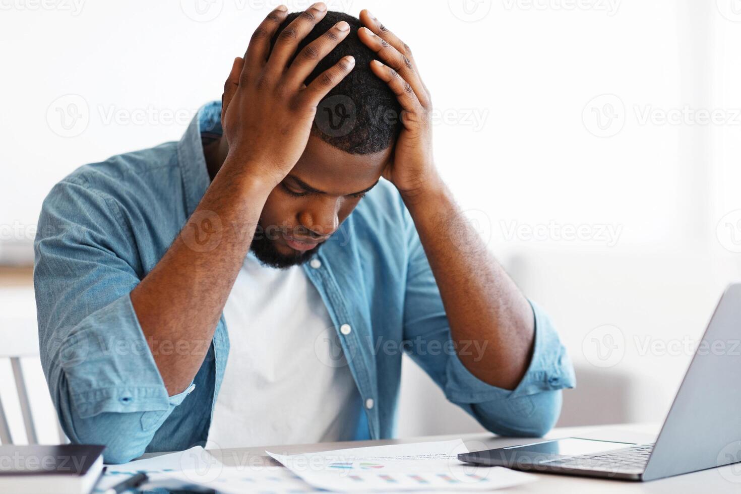 Bankruptcy Concept. Depressed Black Businessman Sitting At Desk With Laptop And Financial Papers And Keeping Head In Hands In Despair, Stressed African Entrepreneur Having Problems At Work, Free Space photo