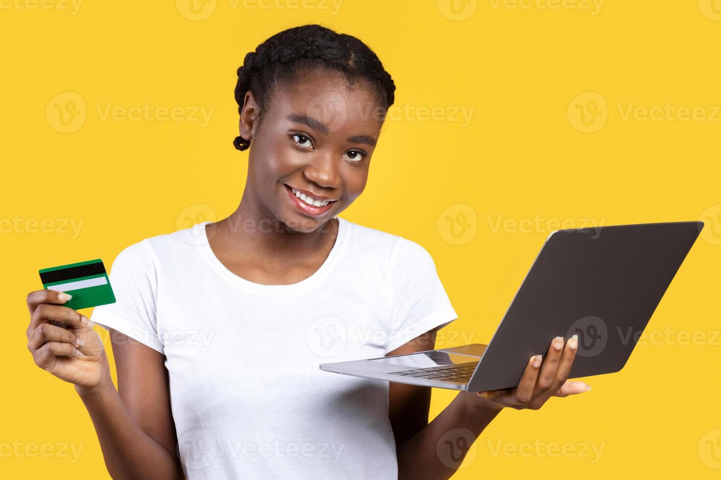 Online Shopping. Happy Black Lady Holding Laptop And Credit Card Posing Smiling To Camera Standing Over Yellow Studio Background. Internet Banking And Payment, Cheerful Customer Concept photo