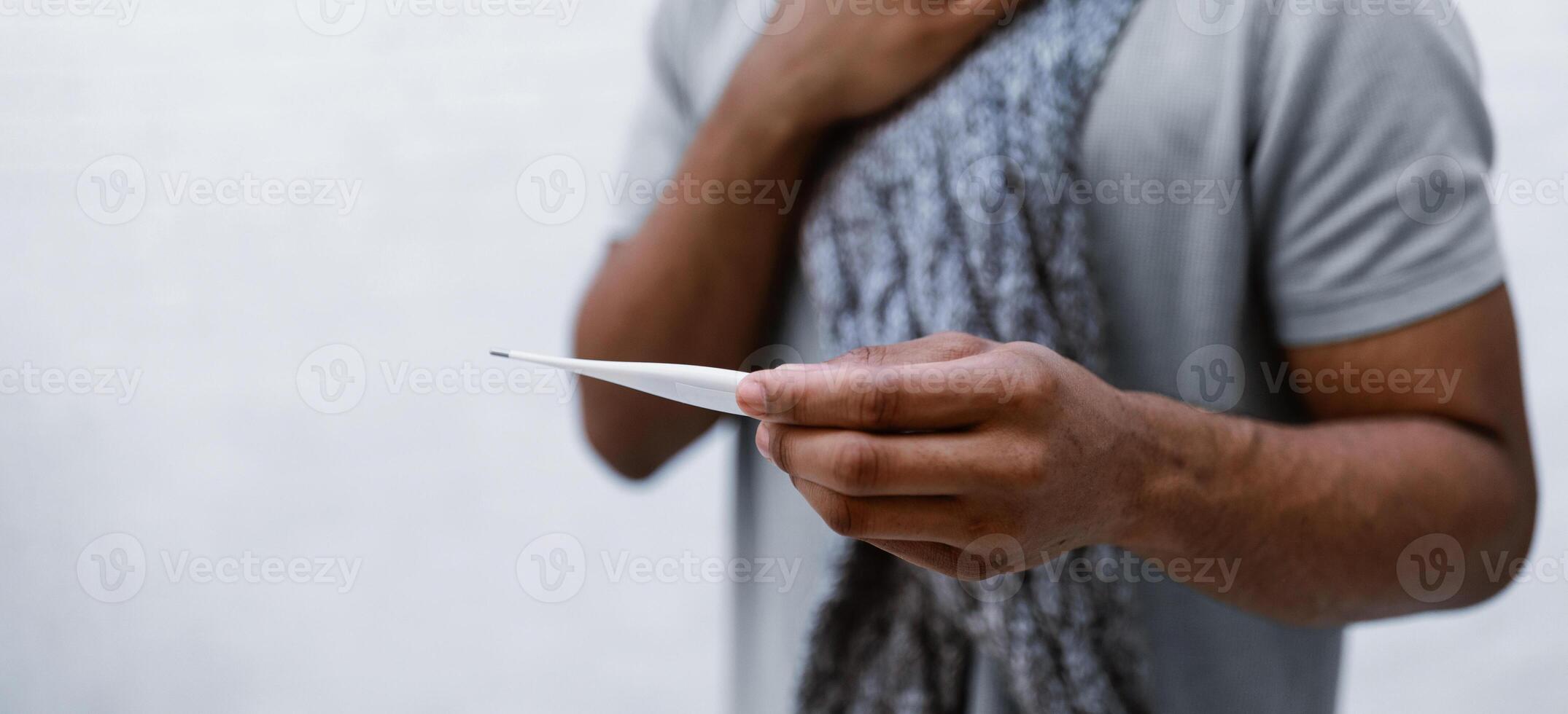 Sick African Man Having Fever Holding Thermometer Suffering From Coronavirus Disease Standing On Gray Studio Background, Touching Aching Throat Having Difficulty Breathing. Cropped, Selective Focus photo