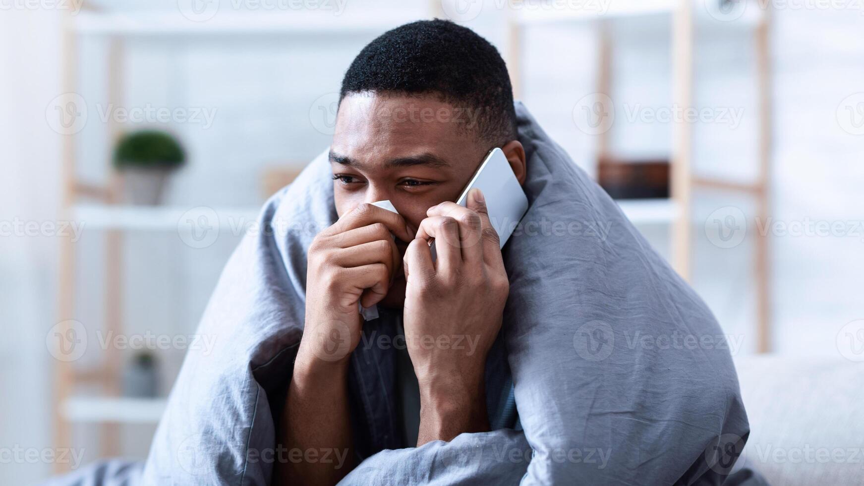 Ill Black Man Calling Doctor Having Runny Nose Suffering From Cold And Rhinitis Sitting On Sofa At Home. Sick African Guy Talking On Phone Feeling Unwell. Symptoms. Influenza Symptoms photo