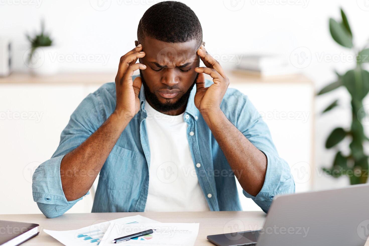 Headache Concept. Stressed Black Man Suffering From Migraine At Workplace, Tired African American Guy Sitting At Desk With Laptop And Touching Temples, Having Strong Pain Or Blood Pressure, Free Space photo