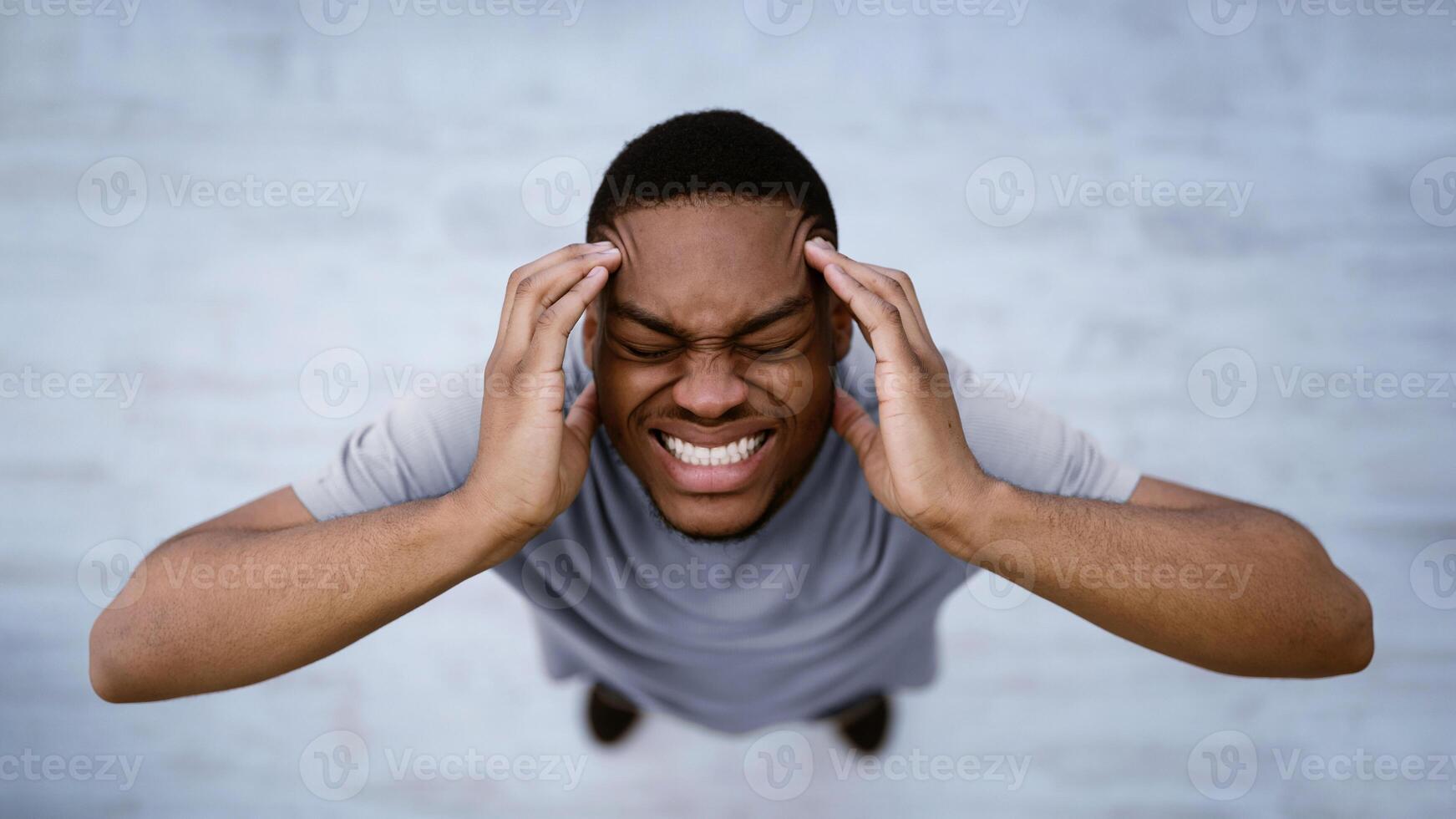 Top View Of Black Man Having Headache Suffering From Migraine Pain, Touching Aching Head Standing Indoors Over Gray Background. Male Health Problem Concept. Panorama, Selective Focus photo