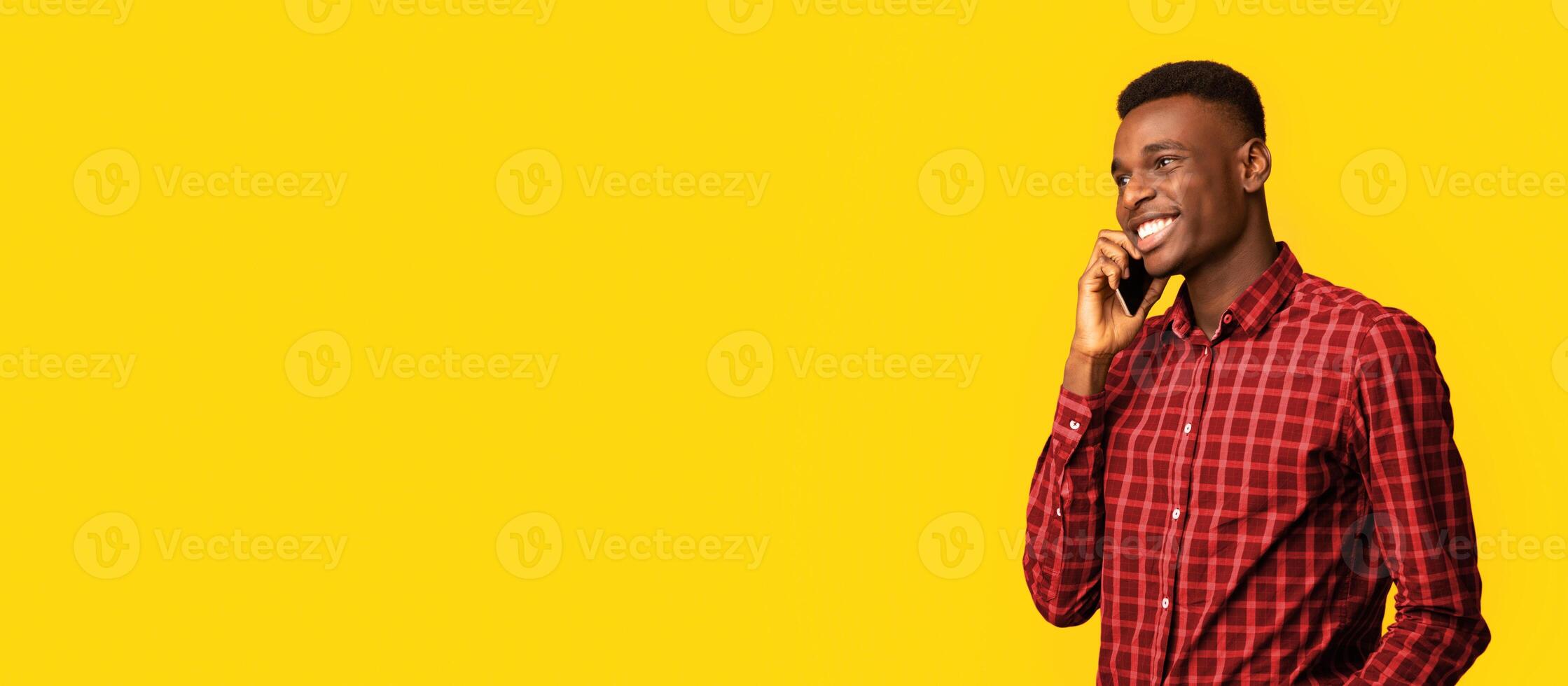 Mobile Communication. Positive African American Guy Talking On Cellphone And Looking Away, Young Black Man Enjoying Pleasant Conversation While Standing Isolated Over Yellow Background, Copy Space photo