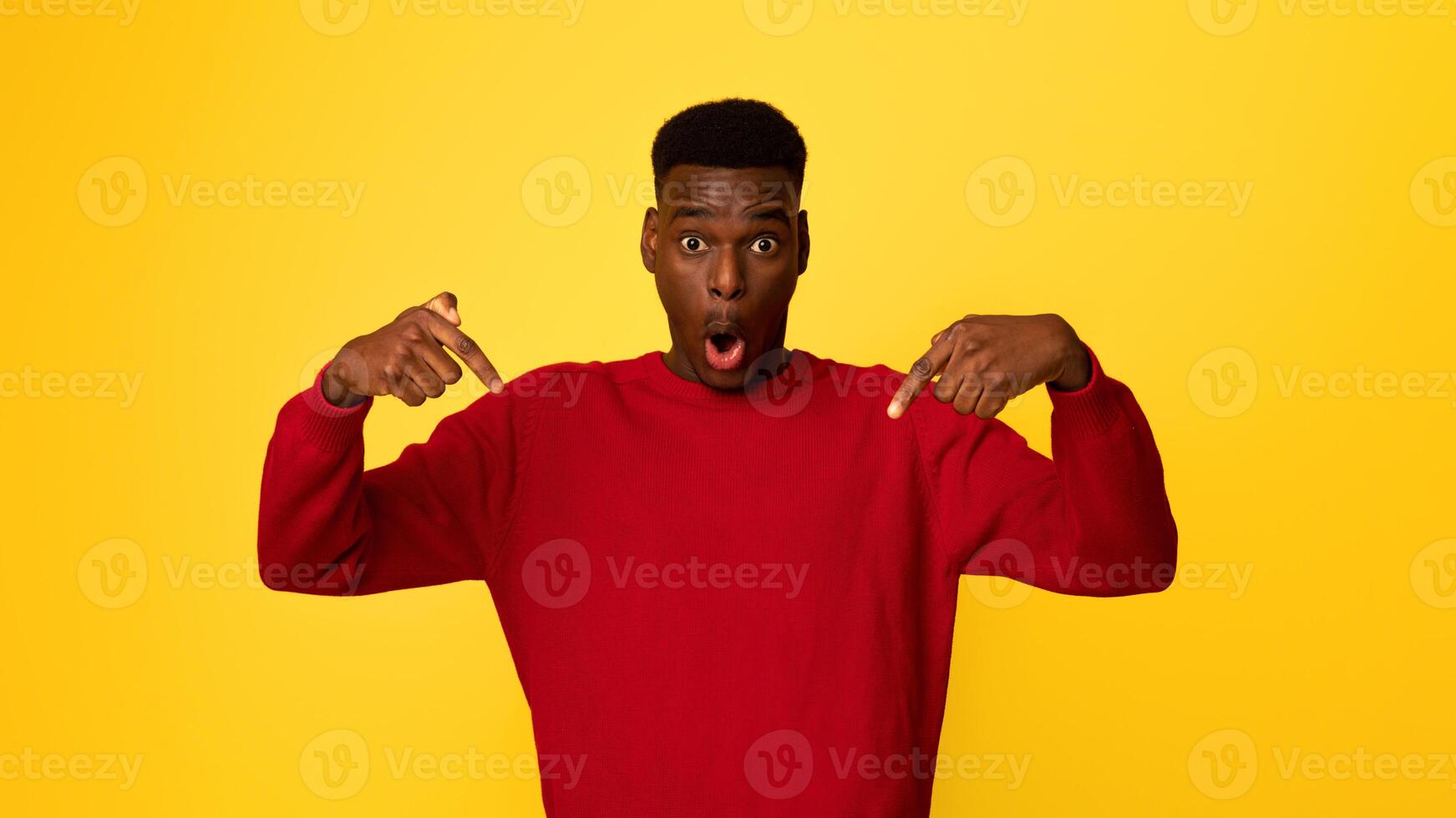 Shocked African American Guy Pointing Down With Fingers, Posing With Open Mouth Over Yellow Studio Background, Emotional Young Black Man In Red Sweater Showing Or Advertising Something, Copy Space photo