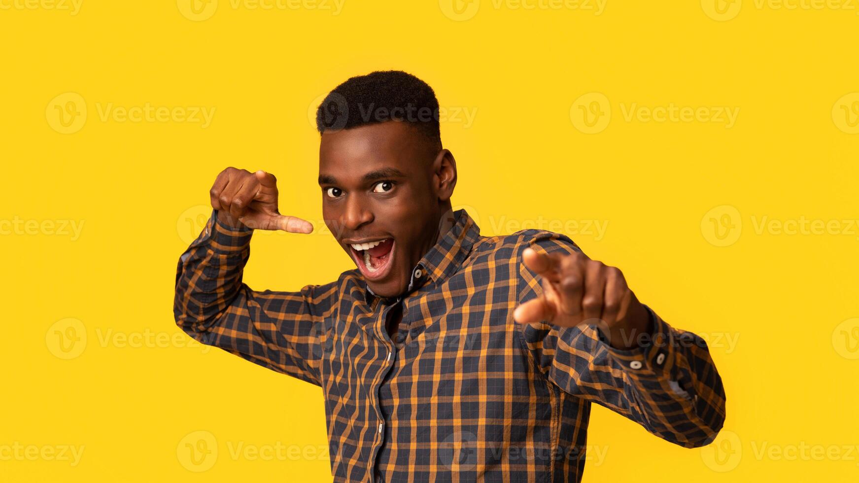 Gotcha. Excited Black Millennial Guy Pointing At Camera With Fingers, Funny Emotional African American Man In Checkered Shirt Indicating Somebody, Standing Isolated Over Yellow Background, Free Space photo