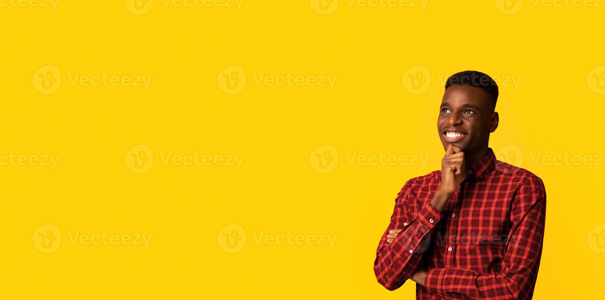 Portraif Of Pensive Dreamy African American Guy Standing Isolated On Yellow Background, Smiling Young Black Man Thinking About Something, Touching Chin And Daydreaming, Panorama With Copy Space photo