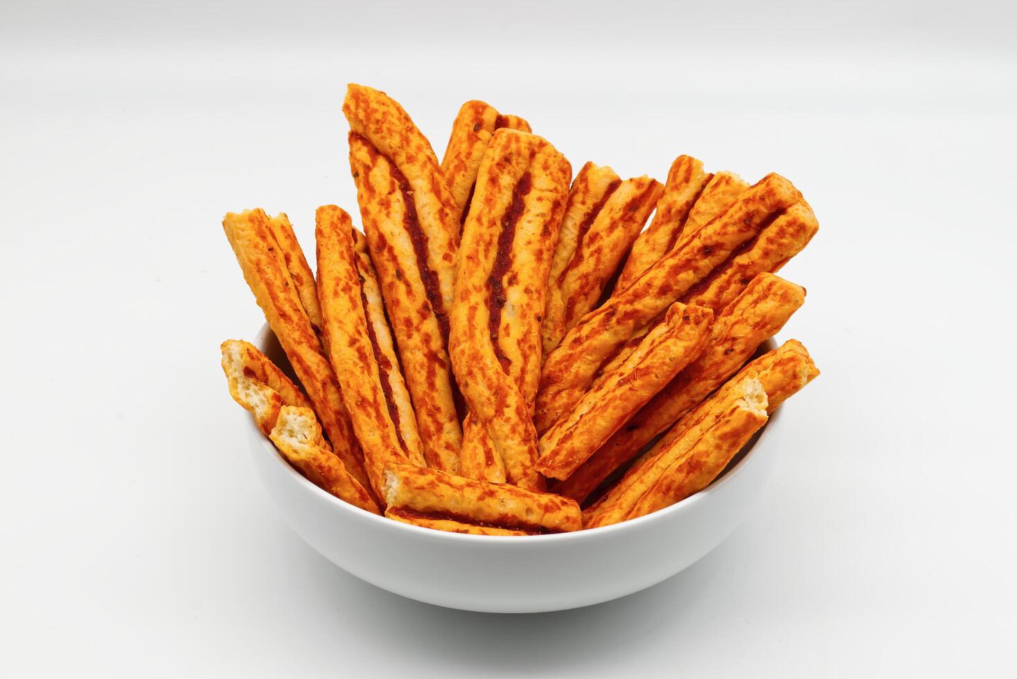 Savory cheese and tomato flavored crispy breadsticks piled high in a white bowl on a clean background. photo