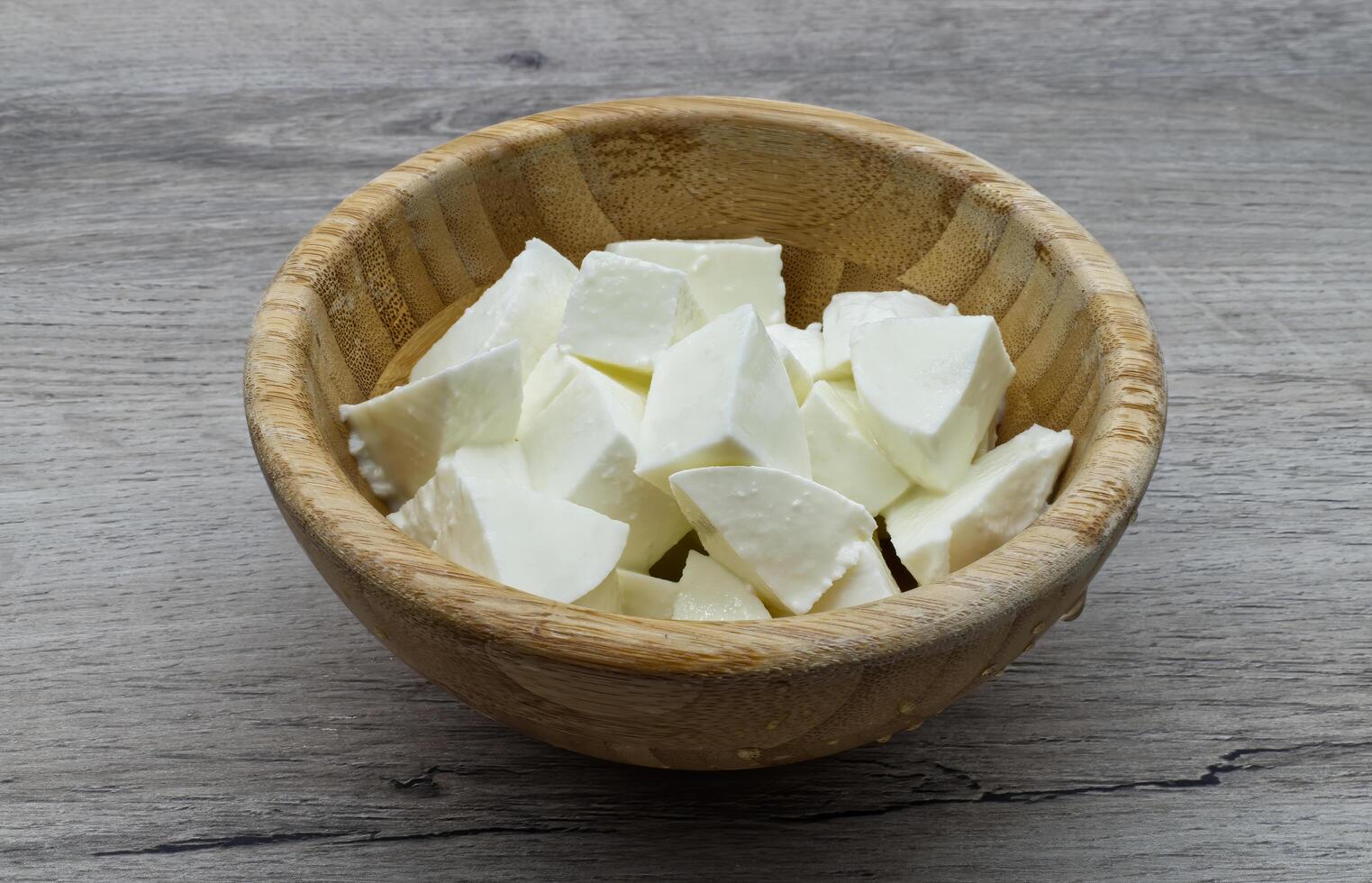 Healthy and fresh soft white cheese pieces served in a small rustic wooden bowl on a wooden table surface photo